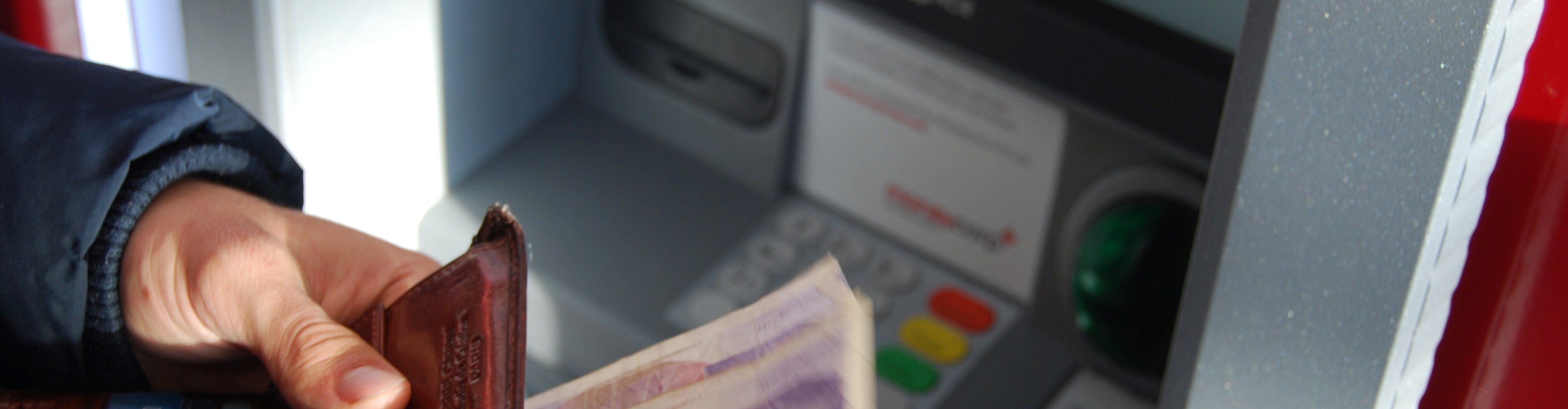 Image of a man holding wallet near atm